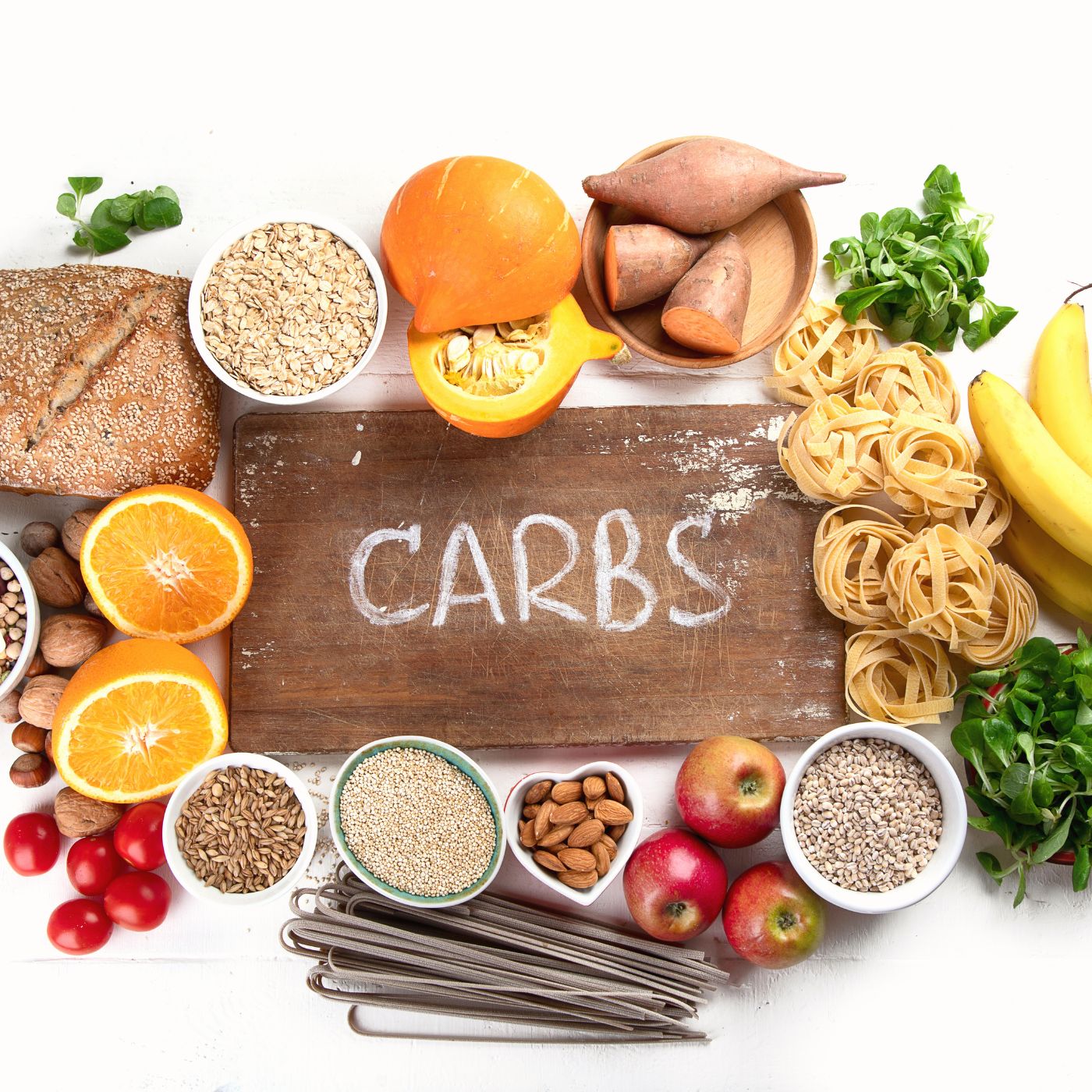 Verschiedene kohlenhydratreiche Lebensmittel liegen um ein Brett, auf welchem "Carbs" geschrieben steht, mythen rund ums abnehmen
